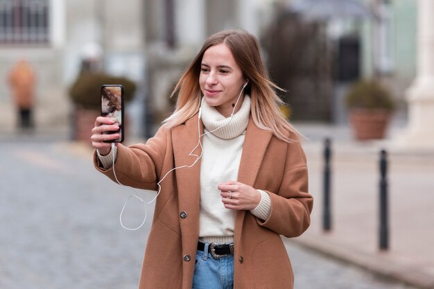 Mujer joven moderna escuchando música en los auriculares mientras toma una selfie