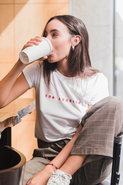 Mujer joven moderna que se sienta en café que bebe el café