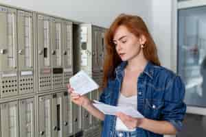 Foto gratuita mujer joven molesta que recibe malas noticias por correo en la entrada del pasillo mujer joven que abre el buzón de correos de pie en el pasillo y sostiene un sobre