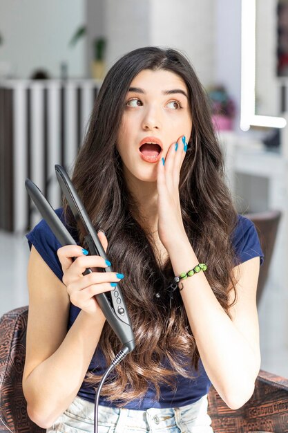 Mujer joven molesta sosteniendo un secador de pelo y llevándose la mano a la cara Foto de alta calidad