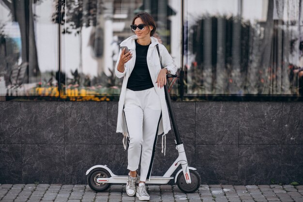 Mujer joven montando scotter en la ciudad y usando el teléfono