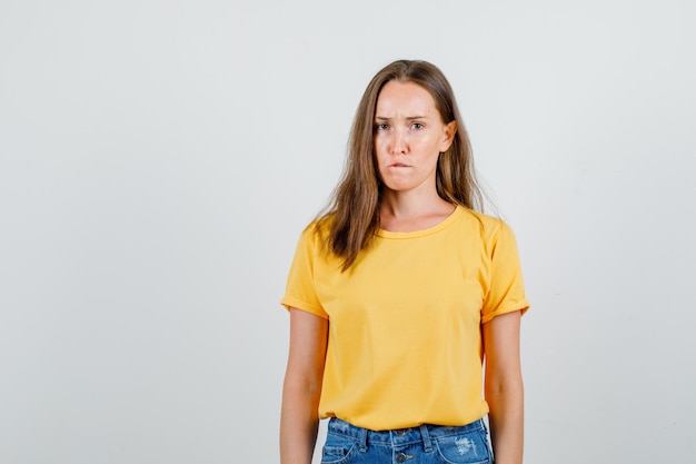 Mujer joven mordiendo el labio en camiseta, pantalones cortos y mirando decepcionado. vista frontal.