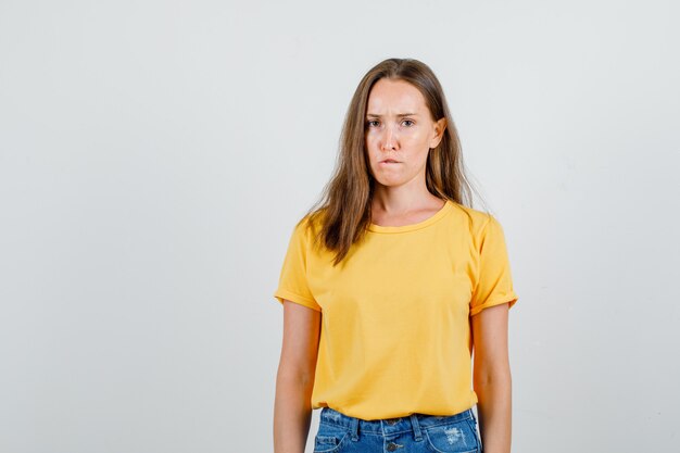 Mujer joven mordiendo el labio en camiseta, pantalones cortos y mirando decepcionado. vista frontal.