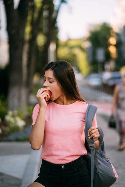 Mujer joven mordiendo la manzana contra un fondo de calle