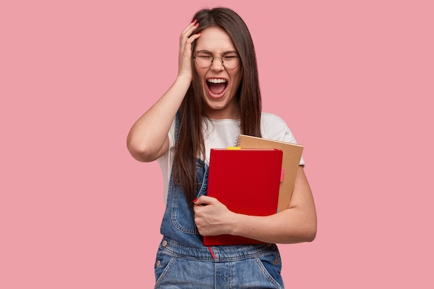 Mujer joven morena en overoles de mezclilla sosteniendo blocs de notas