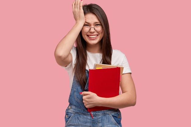 Mujer joven morena en overoles de mezclilla sosteniendo blocs de notas