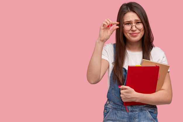 Mujer joven morena en overoles de mezclilla sosteniendo blocs de notas