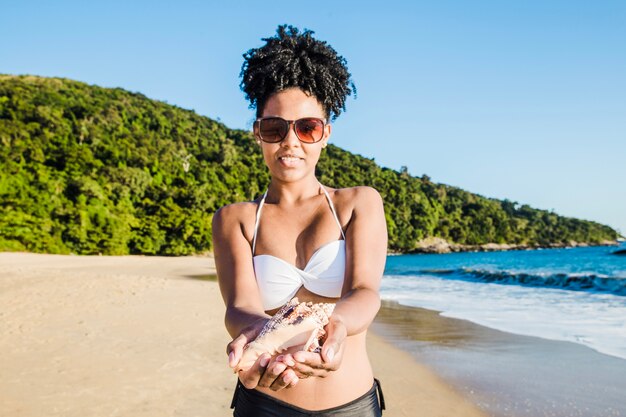 Mujer joven mostrando concha en la playa