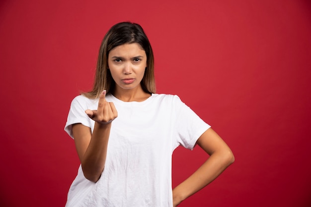 Mujer joven mostrando el dedo y posando en la pared roja.