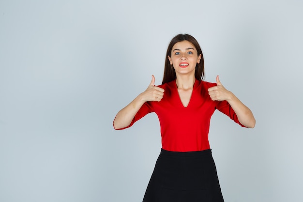 Foto gratuita mujer joven mostrando doble pulgar hacia arriba en blusa roja, falda negra y mirando feliz