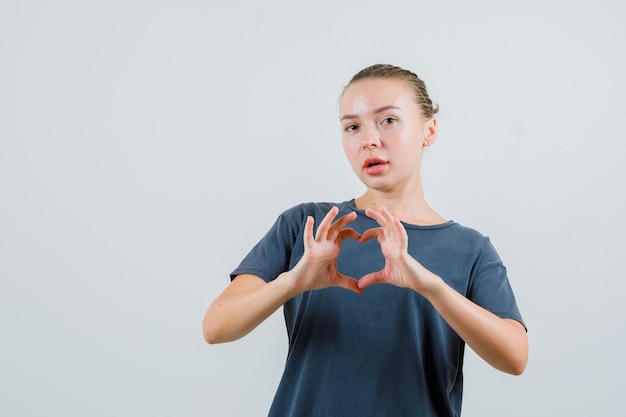 Mujer joven mostrando gesto de corazón en camiseta gris