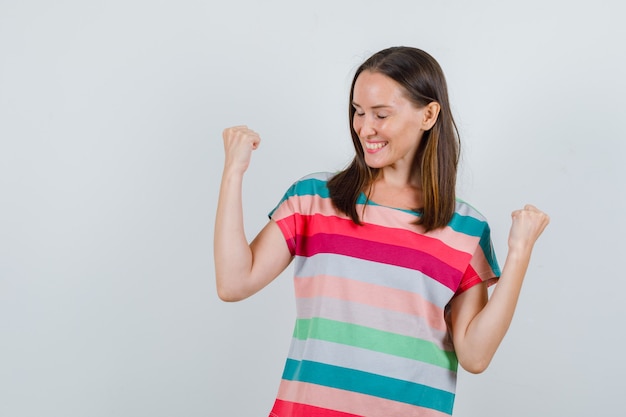 Foto gratuita mujer joven mostrando gesto de ganador en camiseta y mirando feliz, vista frontal.