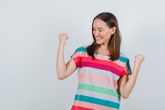 Mujer joven mostrando gesto de ganador en camiseta y mirando feliz, vista frontal.