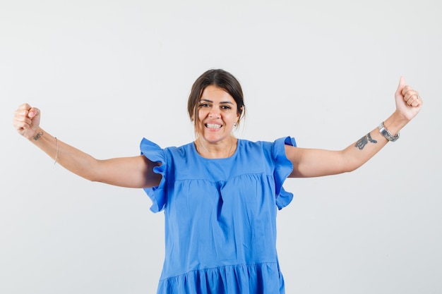 Mujer joven mostrando gesto de ganador en vestido azul y mirando feliz