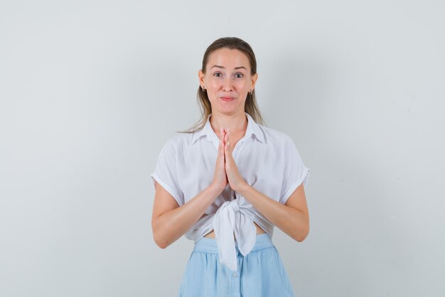 Mujer joven mostrando gesto de namaste en blusa y falda y mirando esperanzado