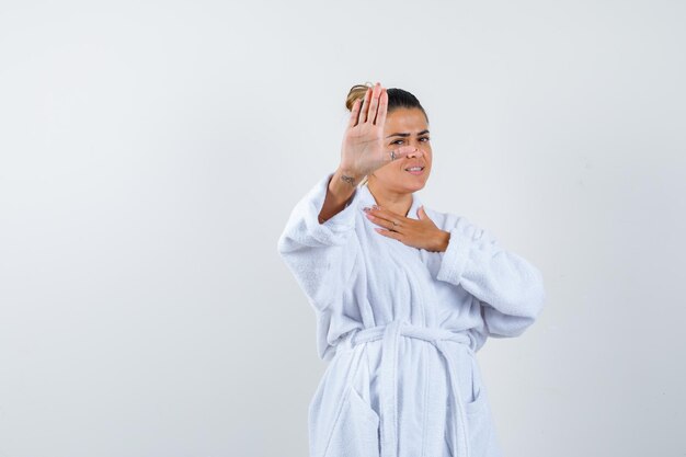 Mujer joven mostrando gesto de parada en bata de baño y mirando confiado