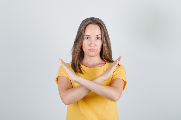 Mujer joven mostrando gesto de parada en camiseta amarilla y mirando agotado
