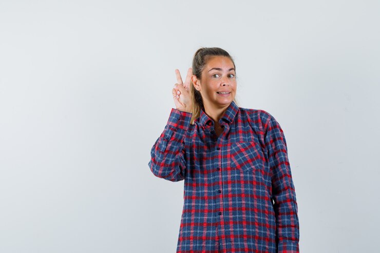 Foto gratuito mujer joven mostrando gesto de paz en camisa a cuadros y bonita