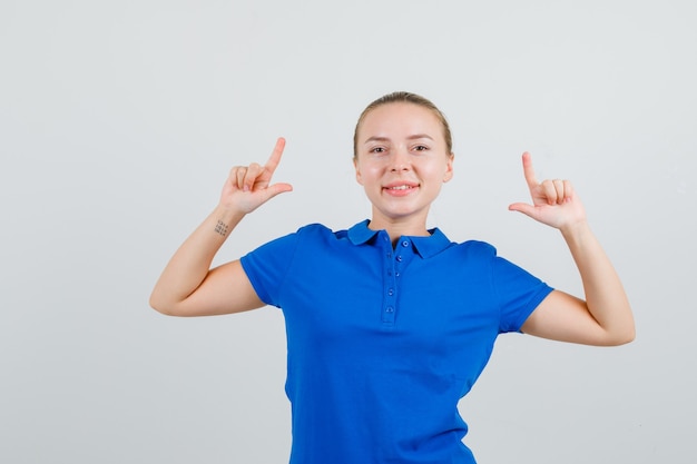 Mujer joven mostrando gesto de pistola en camiseta azul y mirando alegre