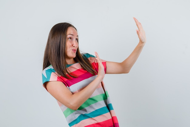 Mujer joven mostrando gesto de rechazo en camiseta y mirando asustado, vista frontal.