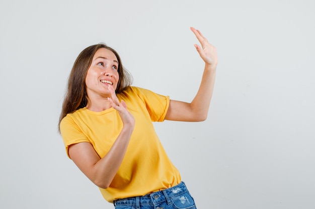 Mujer joven mostrando gesto de rechazo cortésmente en camiseta, pantalones cortos y mirando asustado