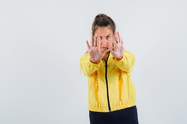 Mujer joven mostrando gesto de rechazo en impermeable amarillo y mirando serio