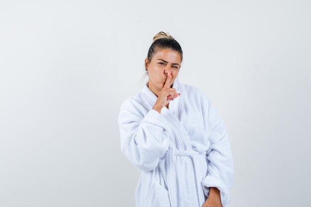 Mujer joven mostrando gesto de silencio en bata de baño y mirando confiado