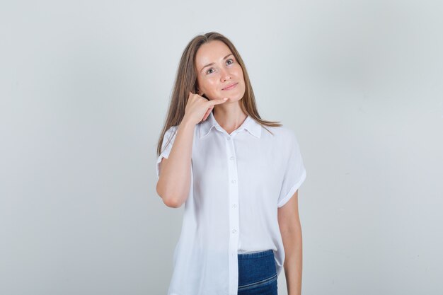 Mujer joven mostrando gesto de teléfono en camiseta, jeans y mirando alegre