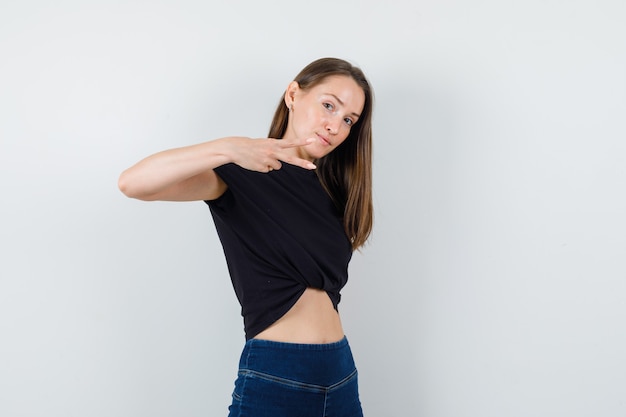 Foto gratuita mujer joven mostrando gesto de tijeras en blusa negra y mirando enfocado
