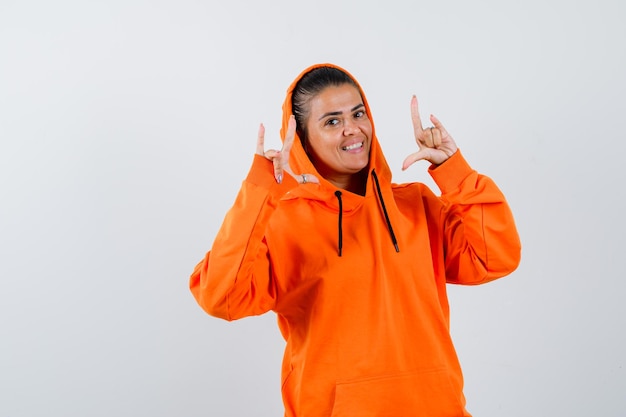 Foto gratuita mujer joven mostrando gestos de rock n roll en sudadera con capucha naranja y luciendo hermosa