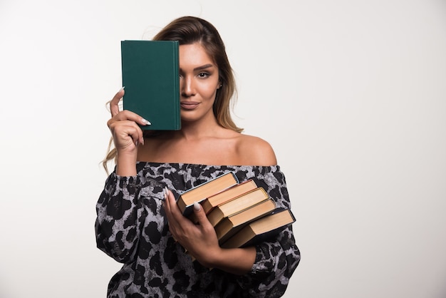 Mujer joven mostrando libros en la pared blanca.