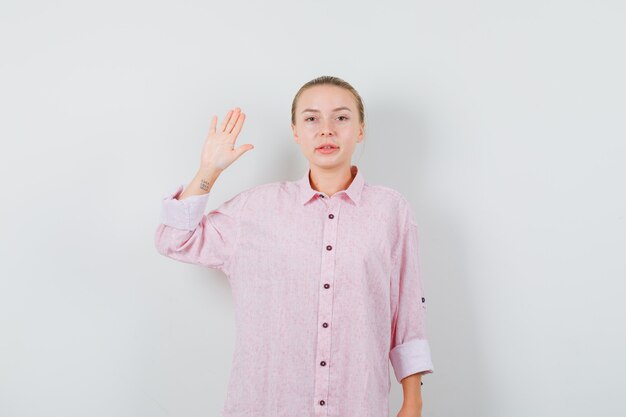 Mujer joven mostrando la palma en camisa rosa y mirando confiado