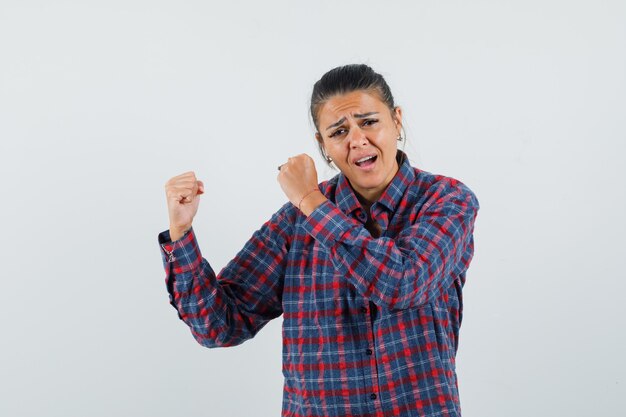 Mujer joven mostrando pose de ganador en camisa a cuadros y mirando emocionado. vista frontal.