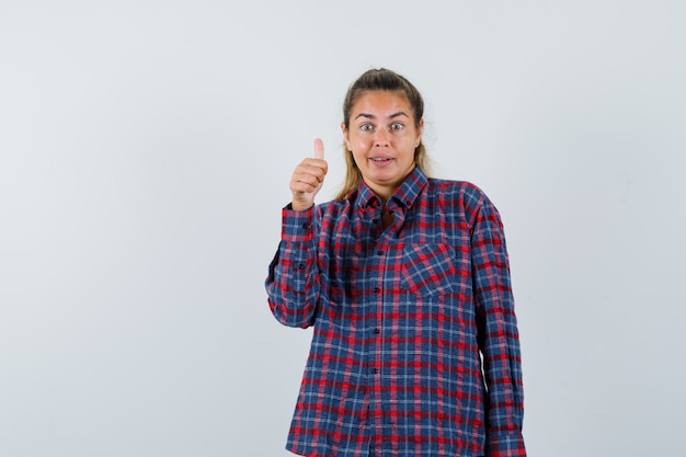 Foto gratuita mujer joven mostrando el pulgar hacia arriba en camisa a cuadros y mirando bastante