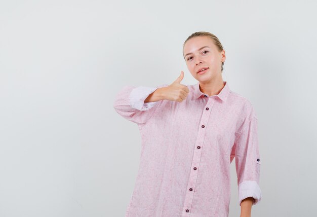 Mujer joven mostrando el pulgar hacia arriba en camisa rosa y mirando complacido