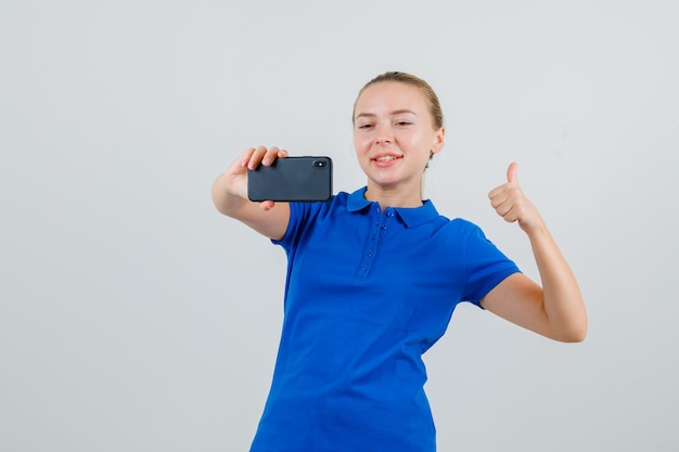 Mujer joven mostrando el pulgar hacia arriba mientras toma selfie en camiseta azul