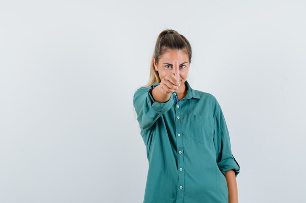 Mujer joven mostrando el pulgar a la cámara con camisa azul y mirando complacido