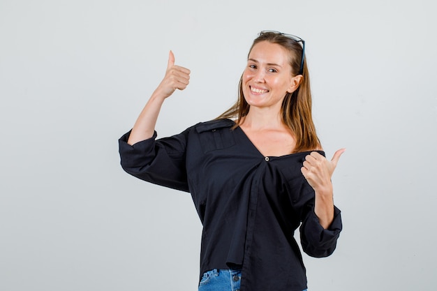 Mujer joven mostrando los pulgares para arriba en camisa, pantalones cortos, gafas y mirando alegre