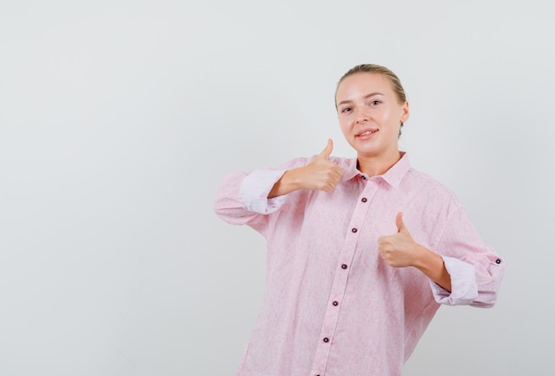 Mujer joven mostrando los pulgares para arriba en camisa rosa y mirando complacido