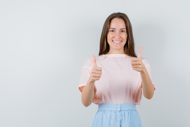 Mujer joven mostrando los pulgares para arriba en camiseta, falda y mirando feliz. vista frontal.