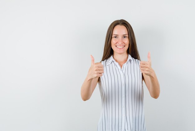 Mujer joven mostrando los pulgares para arriba en camiseta y mirando alegre, vista frontal.