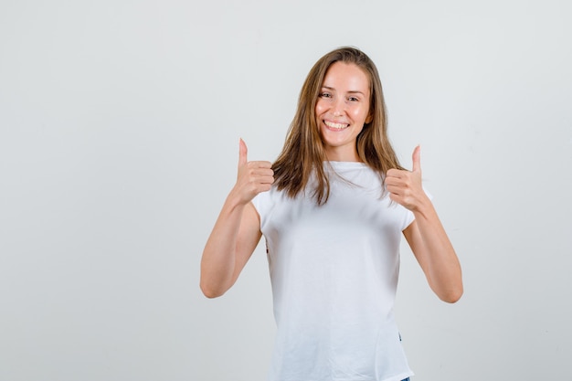 Mujer joven mostrando los pulgares para arriba en camiseta y mirando feliz. vista frontal.