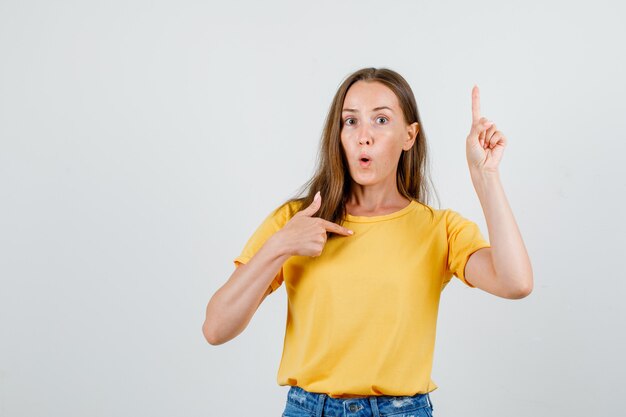 Mujer joven mostrando a sí misma y apuntando hacia arriba en camiseta, pantalones cortos