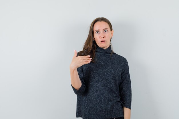 Mujer joven mostrando a sí misma en gesto de perplejidad en camisa