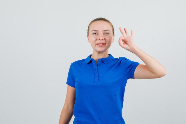 Mujer joven mostrando signo ok en camiseta azul y mirando complacido