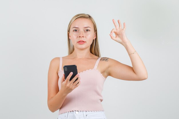 Mujer joven mostrando signo ok y sosteniendo smartphone en camiseta