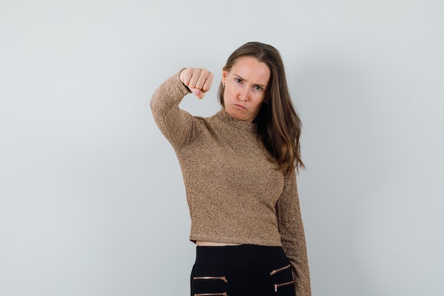 Foto gratuita mujer joven mostrando su puño en blusa dorada y luciendo estricta