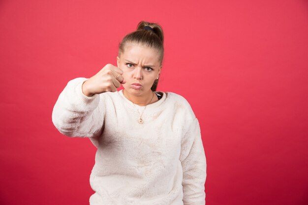 Mujer joven mostrando su puño sobre una pared roja