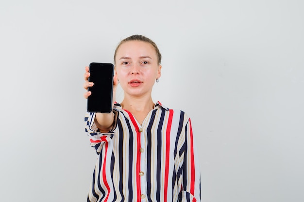 Foto gratuita mujer joven mostrando su teléfono móvil en blusa a rayas y luciendo optimista