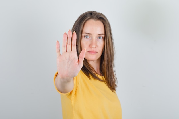 Mujer joven mostrando suficiente gesto con la mano en camiseta amarilla y mirando fatigado